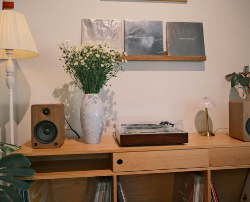Photo of a desk with a vase of flowers and a small speaker and turntable with 3 photos on a floating wall shelf